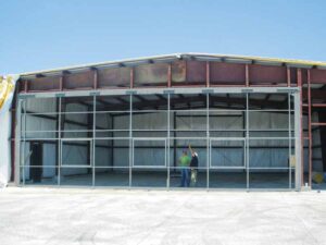 A construction crew member in a hard hat stands in front the all-steel door frame which has just been installed on the front of the hangar. 