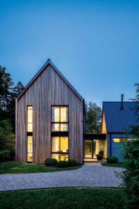 This exterior view of the living room features high ceilings accented by vertical windows and appears well-lit and inviting at dusk. 
