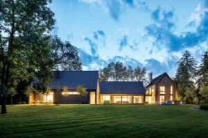 At dusk, a home is brightly lit on the inside, and sits on a well-manicured lawn. 