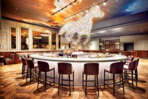The moody lightening showcases a round bar with barstools, and a glass chandelier above the bar in the shape of a horse