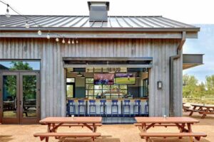A shot of the standing seam metal roof, with the oepn garage style door and entrance to the bar. Picnic tables sit outside the building. 