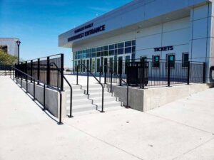 The exterior of a stadium features steps up to the main entrance and the black metal railings. 