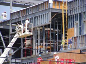 Construction crew on cranes and ladders work on the exterior of a building.