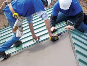 Men in hardhats drill fasteners into metal panels on the roof of a building.
