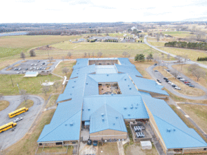 An aerial view of the school as well as surrounding grassy areas, driveways and school buses in the parking lot.