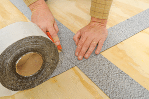A close up of hands cutting seam tape off a role with a blade. 