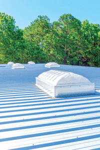 A close-up shot of the skylight on the roof of the wedding venue. Blue sky and tall trees with green leaves are in the background. 