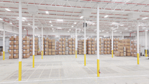 A large, well lit warehouse houses stacks of cardboard boxes. 
