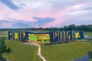On a grassy field sits a rectangular one-story building at dusk. The aluminum exterior features navy blue and green panels.