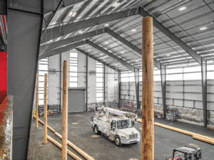 This garage shows a sloped metal ceiling with large wood pillars. A white truck is in the middle of the garage.