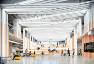 A view of a lounge with open-concept ceilings, brightly lit with natural light, showing employees milling around and relaxing on yellow bean bag style chairs. 