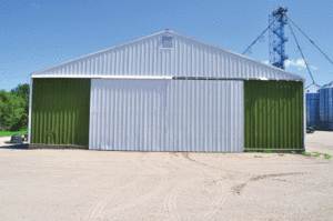 This is the before shot of the front of an airplane hangar with a white roof and door, with green accents on the sides. 