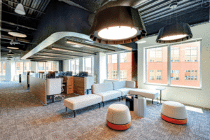 A carpeted lounge area with off-white couches and stools on carpeted floor. 