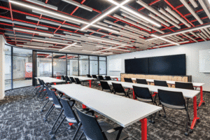 A meeting room features open-concept ceilings with long white tables and black chairs. 