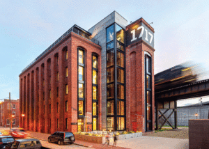 A red brick high rise features new windows with dark metal trim. Elevated train tracks sit behind the building. 