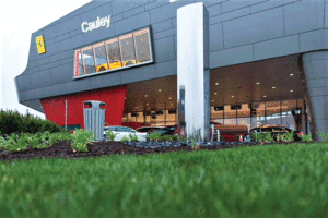 A close up view of the finished dealership, featuring dark grey metal panels over the insulation. In front is lush green grass.