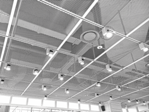 An up-close view of an open concept ceiling with multiple lights, featuring mesh metal panels. 