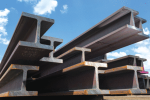 An up-close view of a pile of steel beams with a blue sky with a few clouds in the background.