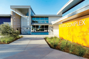 A walkway leads to the outside of a sports complex and shows yellow perforated metal on the right hand side of the walkway. 