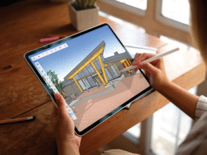 A woman's hands are shown holding a stylus pen, working on a rendering of the exterior of a building on a tablet. 