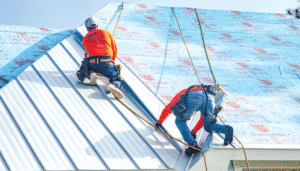 A close-up look at two workers in harnesses, installing insulation and light blue metal panels. 