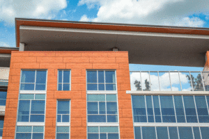 The front of a building is showing glass windows surrounded by orange coloured panels.