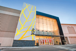 The entrance of the mall features an all glass entrance. To the left of the entrance is a large grey rectangle panel, featuring the outline of a leaf in gold.