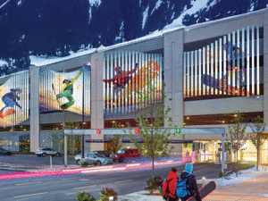 This image shows a close up view of the sunshades on parking garage, which features images of snowboarders in action. There are also snowboarders walking towards the building.