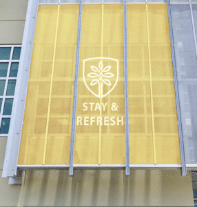 An upward view of a rectangular yellow screen with the words Stay & Refresh below a logo which is an oval-ish type shape with a tree inside. All in white.