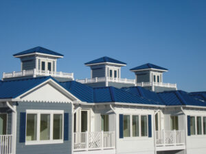 A vertical view of a white house with a dark blue metal roof. A clear blue sky is in the background.