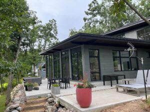 In the backyard, a stone patio surrounds the house. Tall windows make up the rear view. A large red planter sits on the patio. 