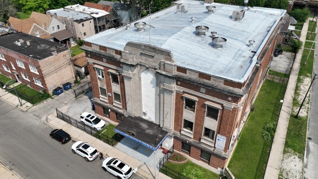 An aerial view of a three-story rectangular red brick structure with metal on the roof.