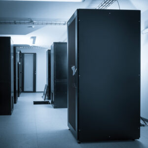 A dimly lit data center, with tall, dark grey metal cabinets housing the servers. 
