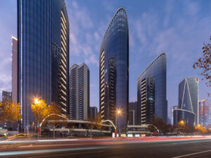 A horizontal image shows three skyscrapers in the foreground at duskl. A street sits in front. 