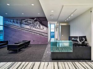 A reception area with a glass desk, white and grey area rugs, and dark grey leather chairs. 