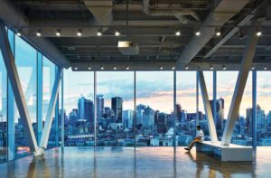 A person sits on a bench in the glass observation deck. The Montreal skyline is in the distance.