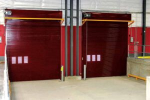 Two side-by-side red rolling doors. Steel pipes are against the wall between them.