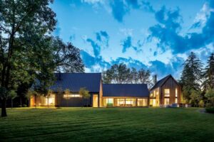 A farmhouse at night with a black metal roof and light wood paneling on the exterior. 