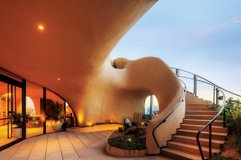 A view of a balcony in the organic facade part of the building. To the left is a glass door and to the right a staircase winds up to the next floor. 
