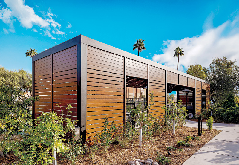 A wall made from metal slats encloses an outdoor sitting area.