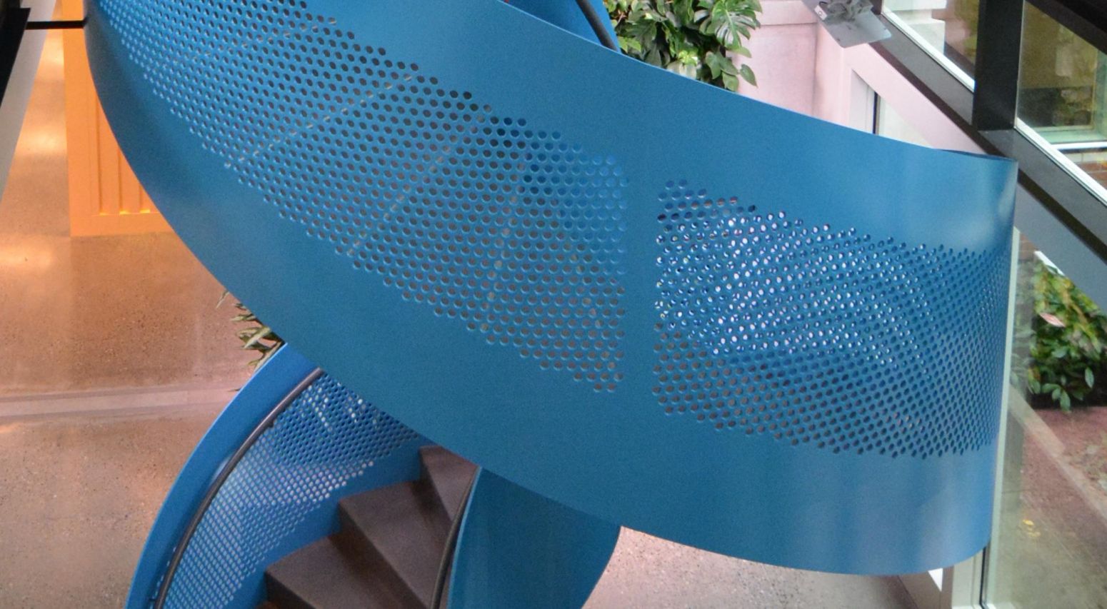 Perforated metal panels wrap arounf a spiral staircase leading into an office building lobby.