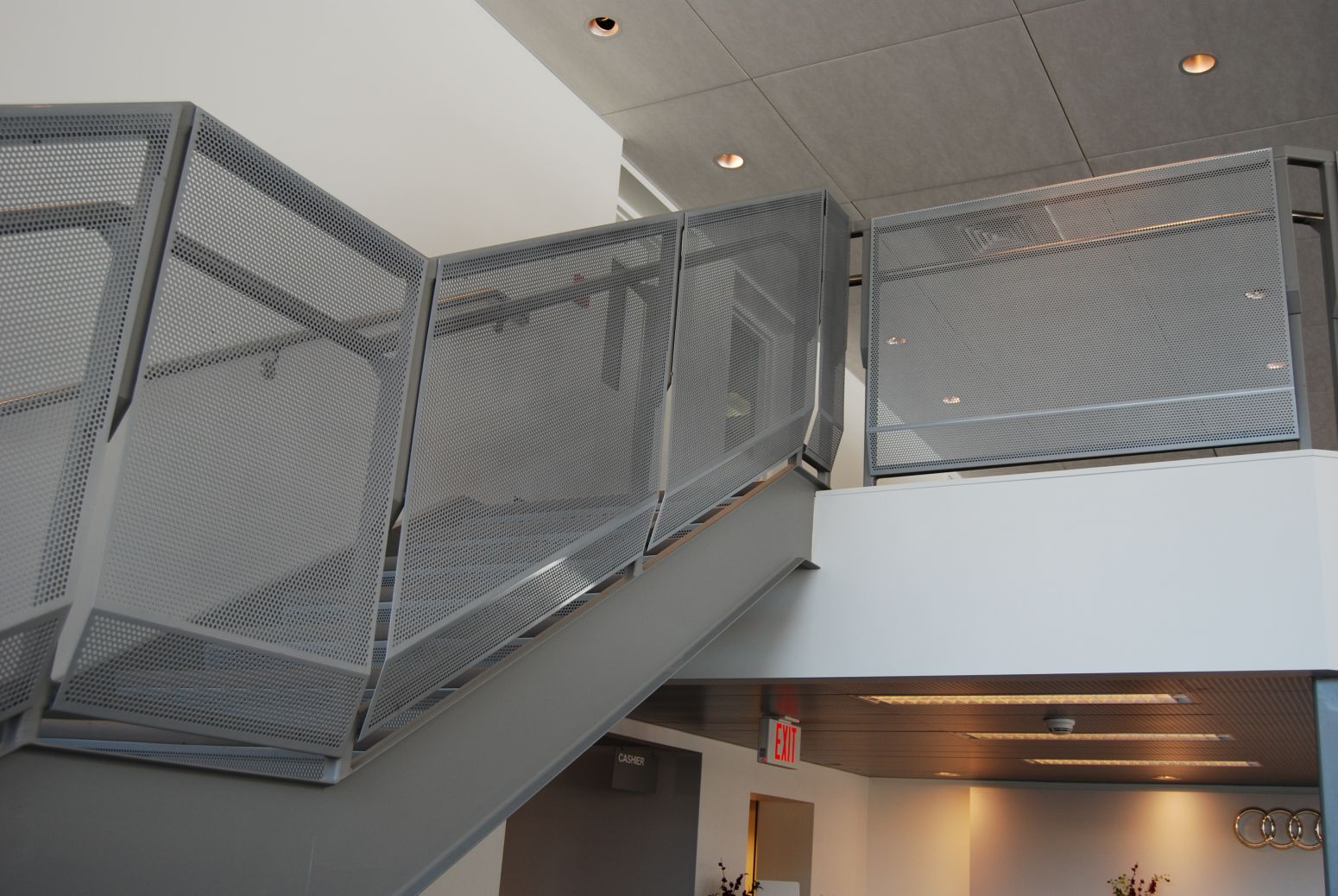 Perforated metal sheets attached to the handrailing of a set of stairs leading up to the second floor of an auto dealership.