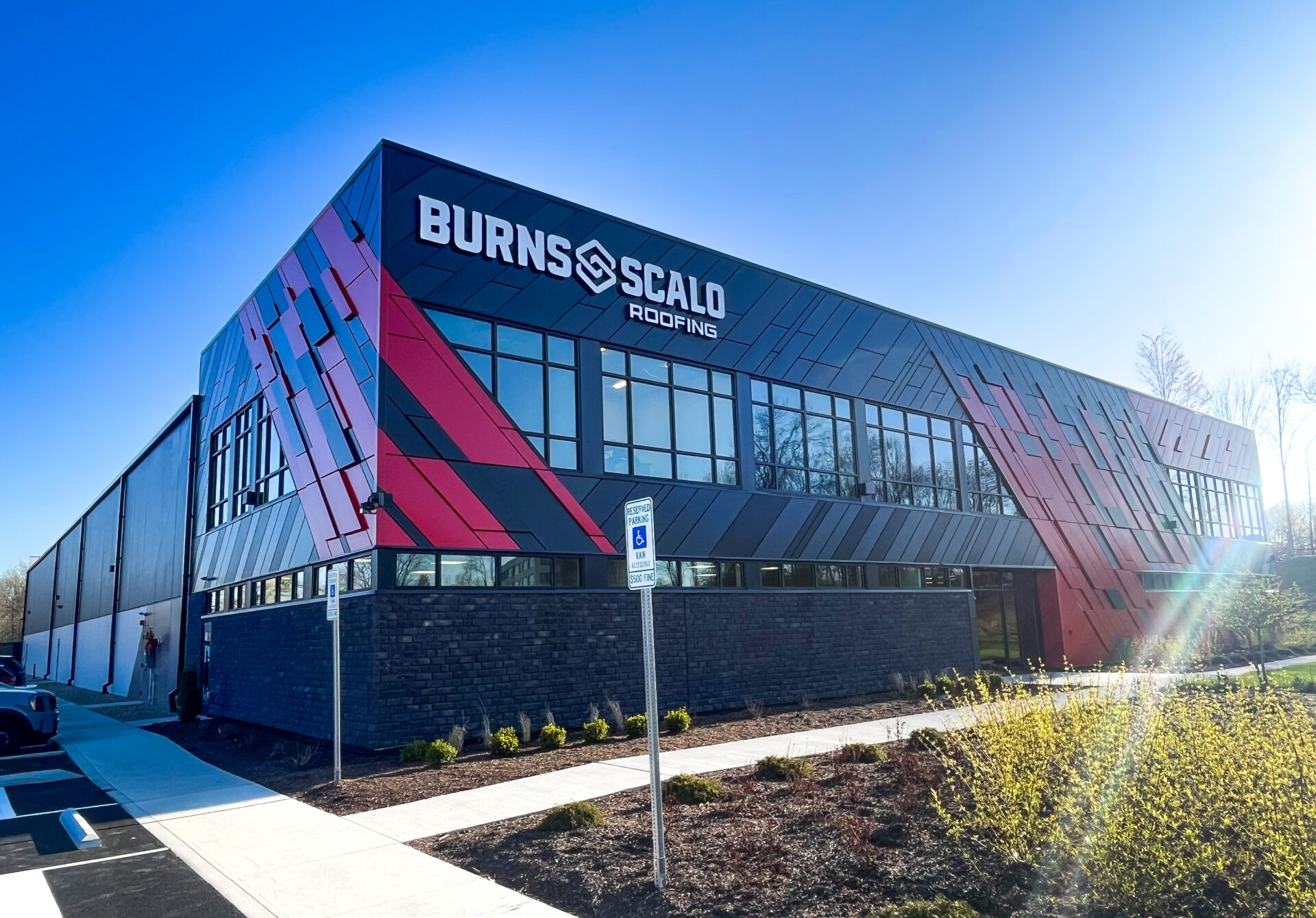 An industrial building has metal panels, including custom, angled ones. Large lettering on the side reads: Burns & Scalo.