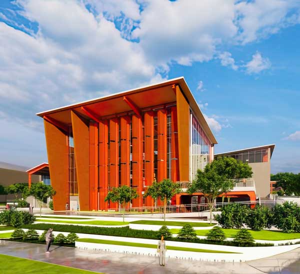 A modern building with bold orange vertical fins and sloped roof, surrounded by green trees, manicured lawns, and a clear blue sky.