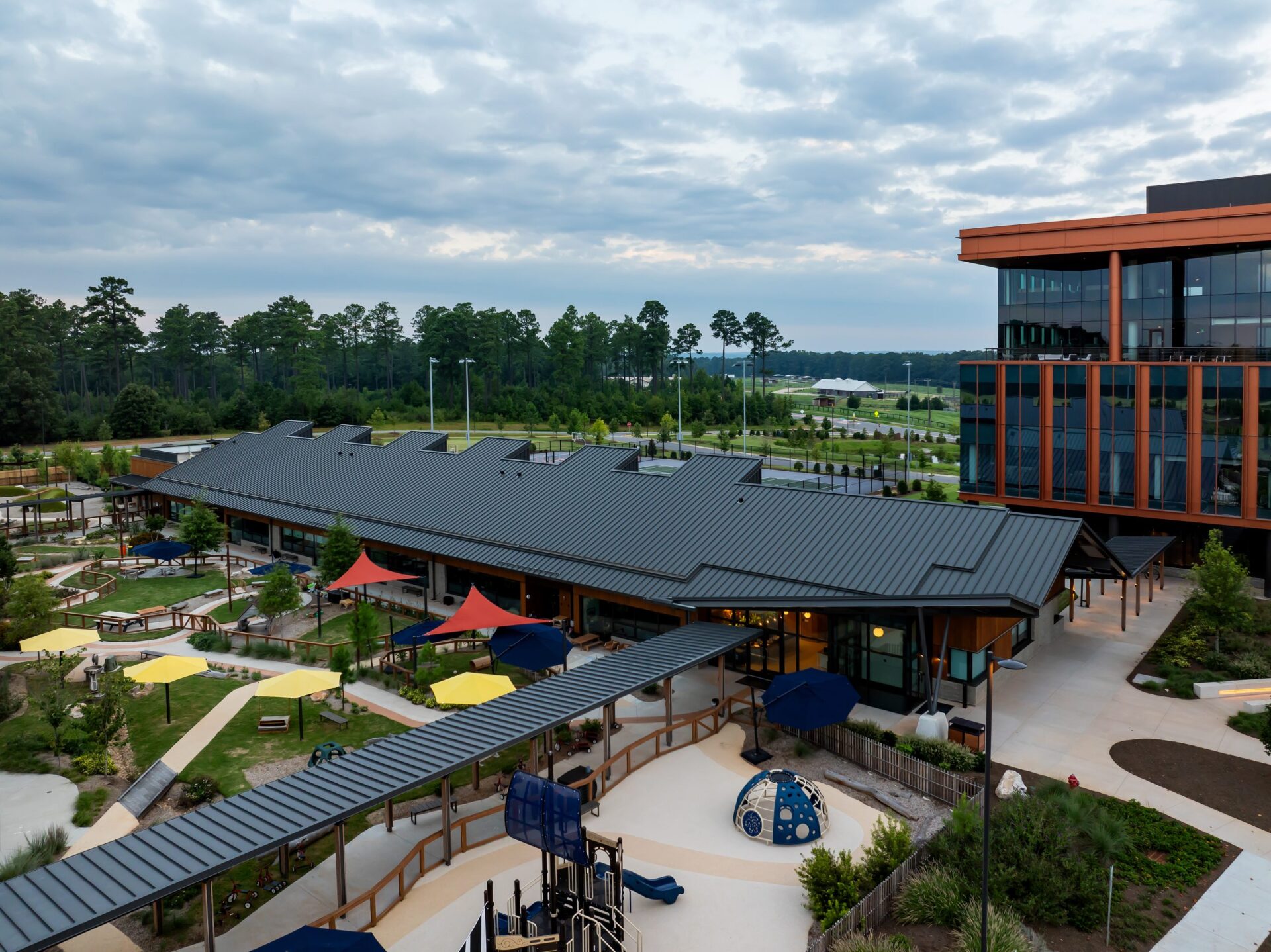 Another view of the office building, with umbrellas in the park and another building in the background.