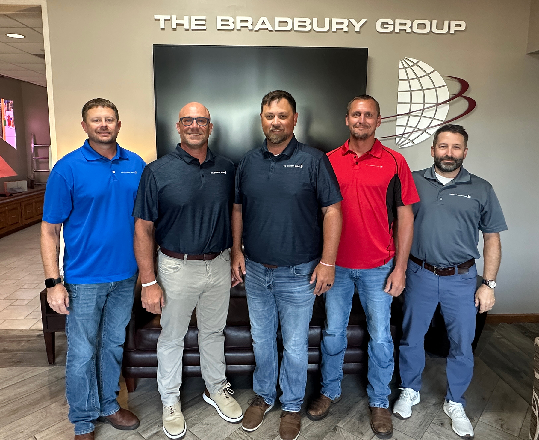 Five male executives stand in front of a television screen. Above them is the logo of The Bradbury Group.