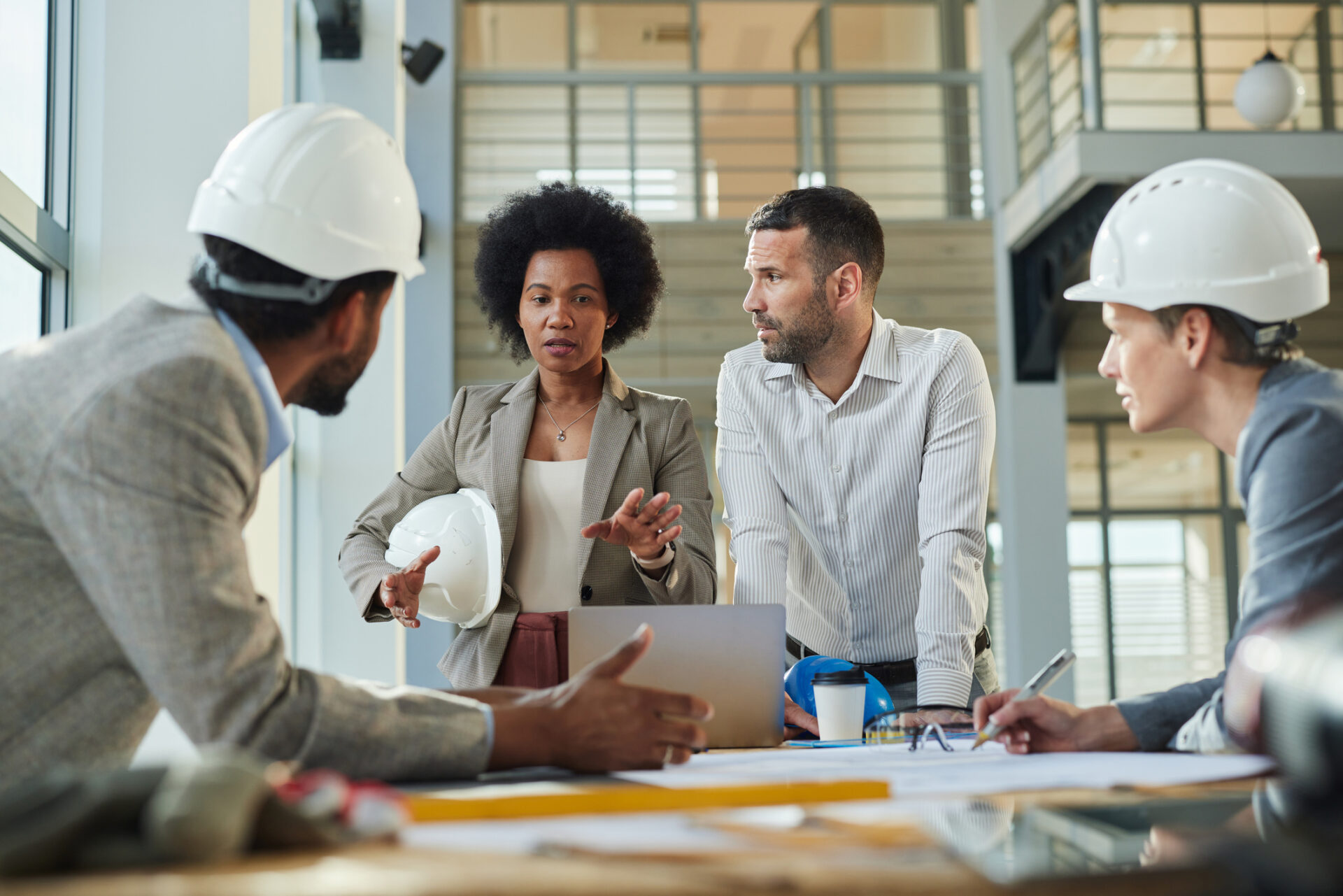 Group of diverse architects communicating while working on blueprints at construction building.