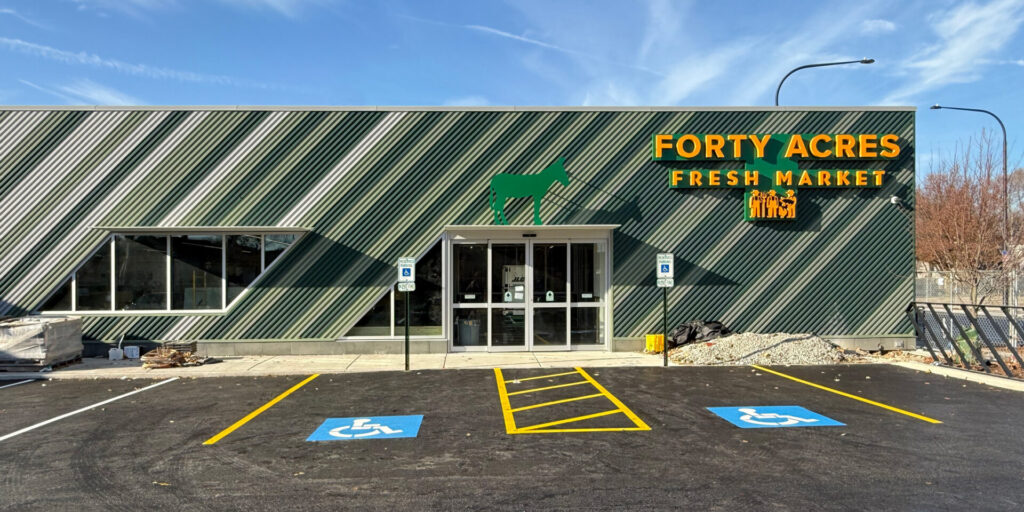 Exterior of Forty Acres Fresh Market with green metal siding, bold yellow signage, and accessible parking spaces.