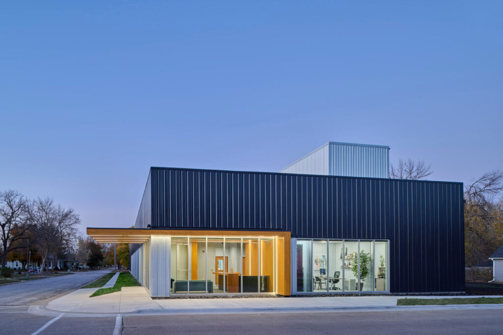 Modern single-story building with black and silver metal cladding, glass storefront, and warm wood-accented entryway.