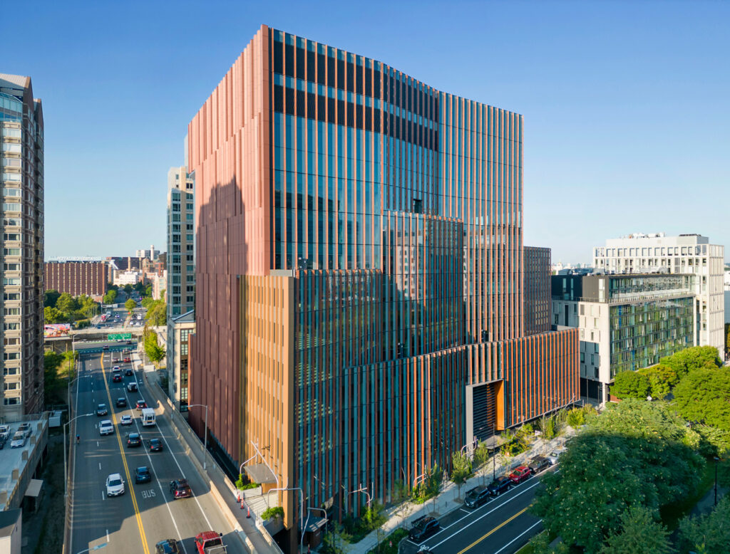 Tall urban building with a copper-toned metal and glass facade, featuring vertical fins and a tiered architectural form.